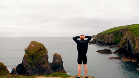 Man-standing-on-cliff-on-a-breezy-day-4k