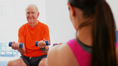 Vista-Trasera-De-Una-Entrenadora-Entrenando-A-Un-Hombre-Mayor-En-Ejercicio-En-El-Gimnasio-4k