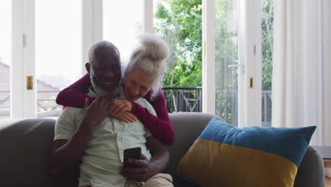 Mixed-race-senior-couple-using-smartphone-in-the-living-room-at-home