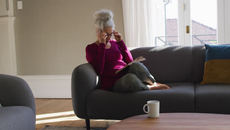 Ältere-Kaukasische-Frau-Liest-Ein-Buch,-Während-Sie-Zu-Hause-Auf-Der-Couch-Sitzt