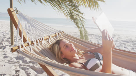 Mujer-Caucásica-Tumbada-En-Una-Hamaca-Y-Usando-Su-Tableta-En-La-Playa