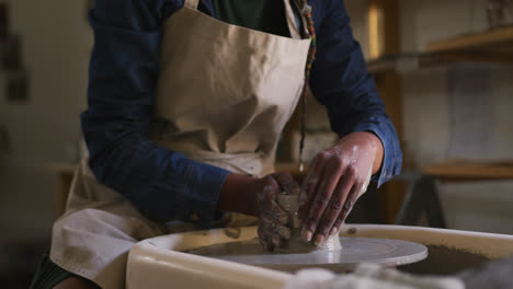 Mid-section-of-female-potter-creating-pottery-on-potters-wheel-at-pottery-studio