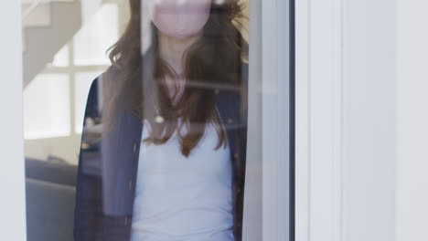 Frau-Mit-Gesichtsmaske-Schaut-Zu-Hause-Aus-Dem-Fenster