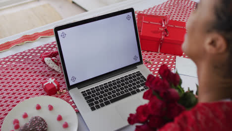 Mixed-race-woman-on-a-valentines-date-video-call,-holding-pink-roses