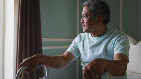 Senior-mixed-race-man-with-walking-frame-looking-out-of-window