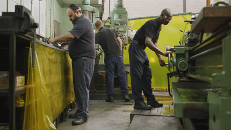 Caucasian-and-African-American-male-factory-worker-standing-at-a-workbench-and-operating-machinery