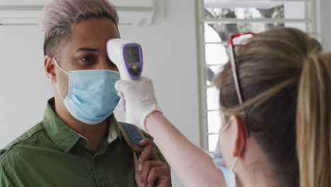 Man-wearing-face-mask-getting-his-temperature-measured-at-office