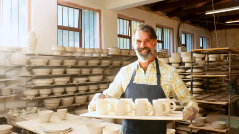 Happy-male-potter-holding-ceramic-cups-in-tray-4k