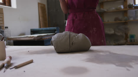 Mid-section-of-female-potter-cutting-clay-with-thread-at-pottery-studio