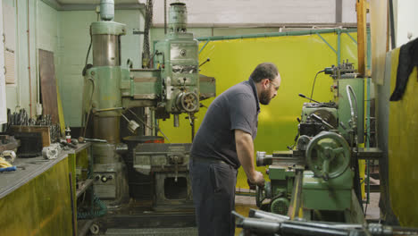 Caucasian-male-factory-worker-at-a-factory-sitting-at-a-workbench-and-operating-machinery-