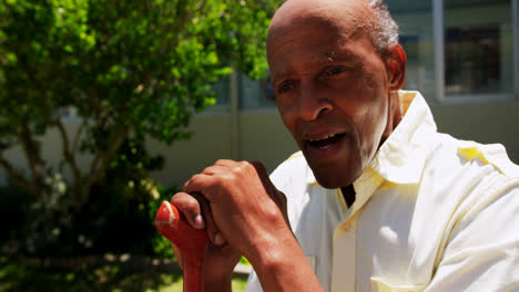 Front-view-of-active-Asian-senior-man-sitting-with-walking-stick-in-the-garden-of-nursing-home-4k