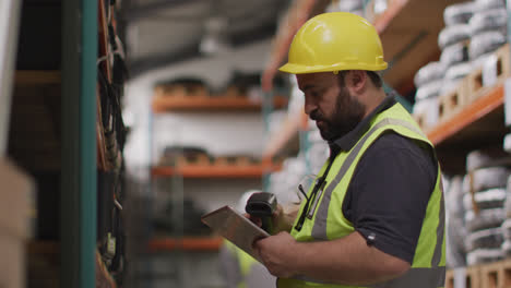 Caucasian-male-factory-worker-at-a-factory-wearing-a-hard-hat-and-high-vis-vest,-checking-stock-