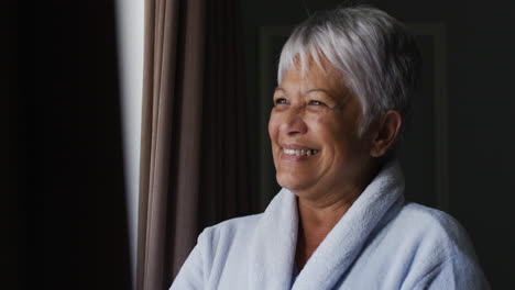 Senior-mixed-race-woman-at-home-waving-out-of-window