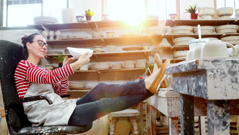 Female-potter-checking-bowl-while-relaxing-on-chair-4k