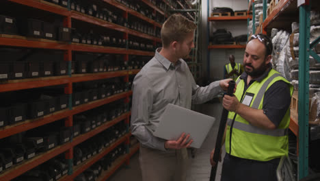 Two-Caucasian-male-factory-workers-at-a-factory-wearing-vis-vest-and-holding-a-pipe,-standing-