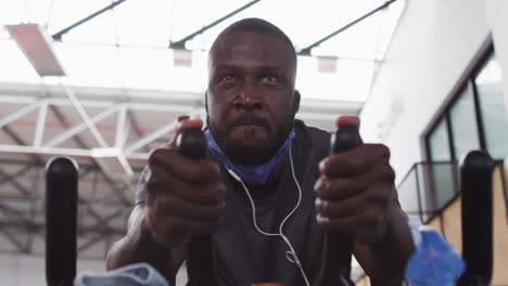 African-american-man-wearing-lowered-face-mask-exercising-at-gym