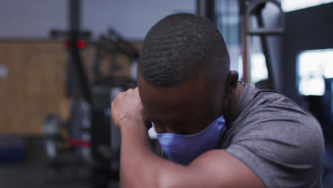 Hombre-Afroamericano-En-Forma-Con-Mascarilla-Estornudando-En-El-Codo-En-El-Gimnasio