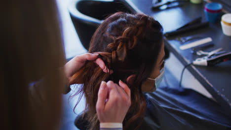 Peluquera-Trenzando-El-Cabello-De-Una-Clienta-Usando-Mascarilla-En-La-Peluquería