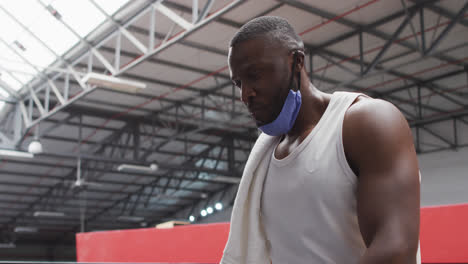 African-american-man-wearing-lowered-face-mask-drinking-at-gym