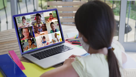 Caucasian-schoolgirl-in-face-mask-using-laptop-on-video-call-with-school-friends