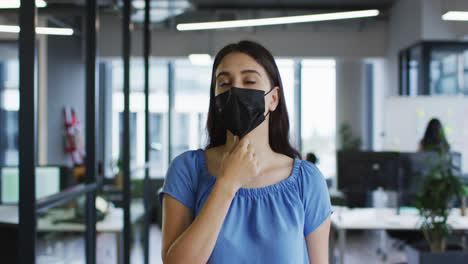 Porträt-Einer-Kaukasischen-Geschäftsfrau,-Die-Im-Büro-Steht-Und-Die-Gesichtsmaske-Anpasst-Und-In-Die-Kamera-Blickt