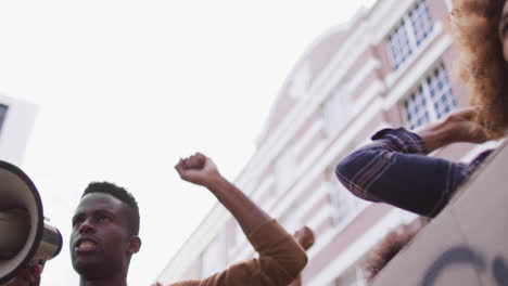 Hombre-Afroamericano-Gritando-Usando-Megáfono-Con-Otras-Personas-Levantando-Puños-Durante-La-Protesta