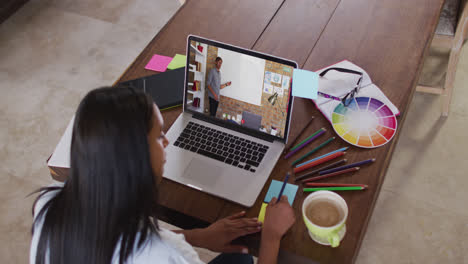 Caucasian-female-student-using-laptop-on-video-call-with-male-teacher,-making-notes