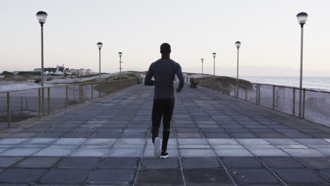 Back-view-of-african-american-man-exercising-outdoors,-running-by-seaside