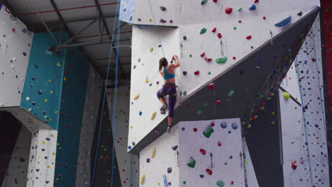 Caucasian-woman-wearing-face-mask-climbing-wall-at-indoor-climbing-wall