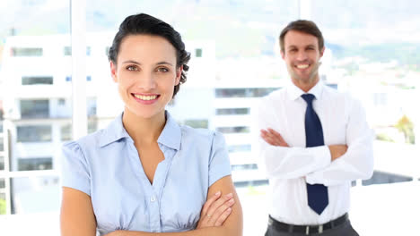 Pretty-businesswoman-smiling-at-camera-with-colleague-behind-her