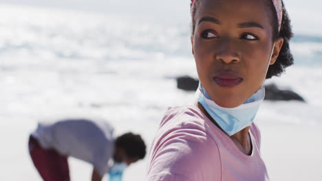 Mujer-Afroamericana-Con-Mascarilla-Tomando-Un-Descanso-De-Recoger-Basura-De-La-Playa