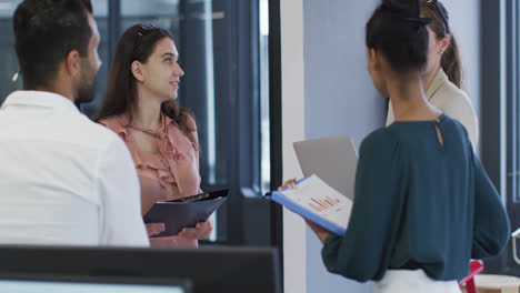 Caucasian-businesswoman-holding-file-talking-to-diverse-colleagues-at-casual-office-meeting