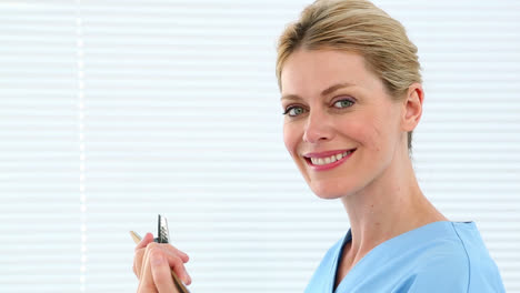 Blonde-nurse-holding-clipboard-smiling-at-camera