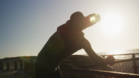 Hombre-Afroamericano-Bebiendo-Agua,-Tomando-Un-Descanso-En-El-Ejercicio-Al-Aire-Libre-Junto-Al-Mar