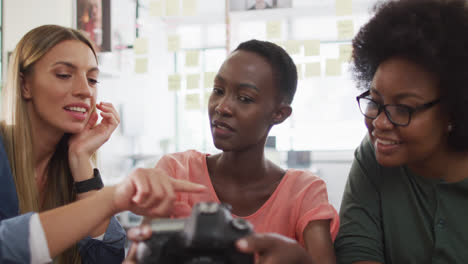 Three-diverse-female-colleagues-in-discussion-sitting-looking-at-images-on-camera-in-office