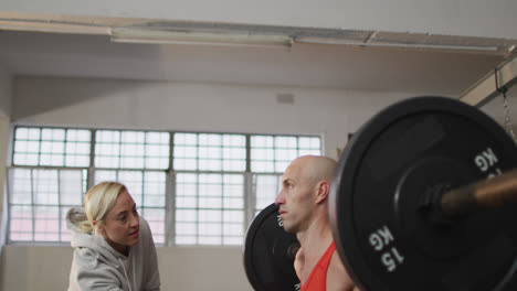 Caucasian-muscular-man-lifting-weight-bar-with-female-coach