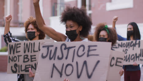 Diverse-group-of-men-and-women-holding-placards-shouting-raising-fists-during-protest-wearing-masks