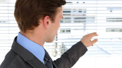 Businessman-peeking-through-roller-blind-and-smiling-at-camera