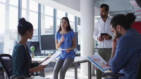 Caucasian-businesswoman-holding-file-and-talking-to-diverse-colleagues-at-casual-office-meeting