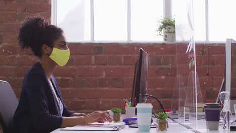 Mujer-De-Negocios-De-Raza-Mixta-Escribiendo-Sentada-Frente-A-La-Computadora-Usando-Máscara-Facial