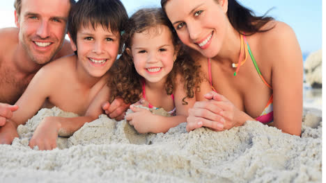 Portrait-of-smiling-caucasian-family-on-holiday-lying-on-sand-by-sea