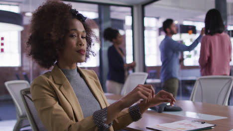 Mixed-race-businesswoman-sitting-smiling-in-meeting-room-with-diverse-colleagues-in-background