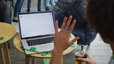 Frau-Mit-Gemischter-Abstammung-Feiert-St.-Patrick&#39;s-Day-Und-Macht-Videoanruf-Mit-Laptop-In-Einer-Bar