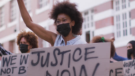 Diverse-group-of-men-and-women-holding-placards-shouting-raising-fists-during-protest-wearing-masks