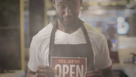 Animación-De-Destellos-De-Lente-Y-Luz-Solar-Con-Un-Comerciante-Sosteniendo-Un-Cartel-Abierto-Y-Sonriendo