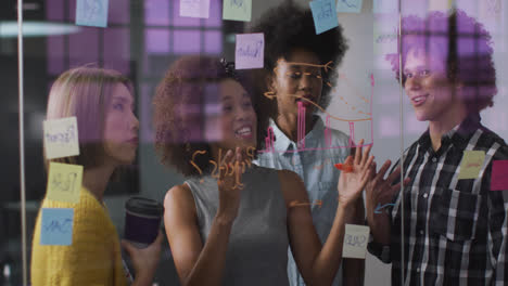 Diverse-work-colleagues-writing-and-drawing-on-glass-wall-having-a-discussion