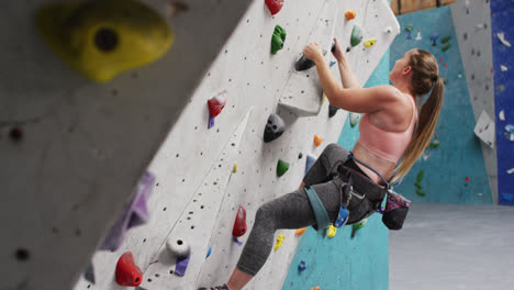 Caucasian-woman-wearing-face-mask-climbing-wall-at-indoor-climbing-wall