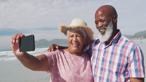 Mixed-race-senior-couple-taking-a-selfie-with-a-smartphone-at-the-beach