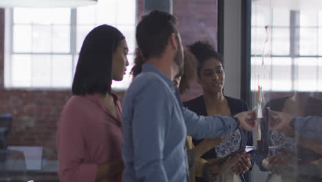 Diverse-colleagues-using-memo-notes-on-glass-wall-having-a-discussion