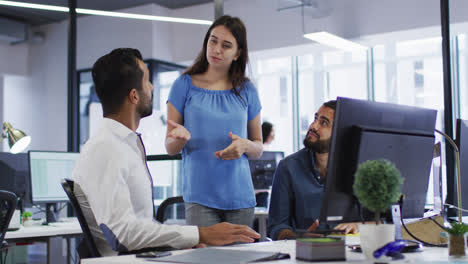 Caucasian-businesswoman-standing-in-discussion-with-two-mixed-race-male-colleagues-at-their-desk